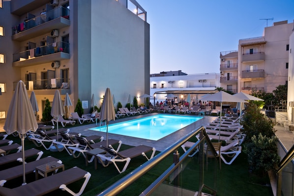 A rooftop pool area with sun loungers, umbrellas, and a bar area.
