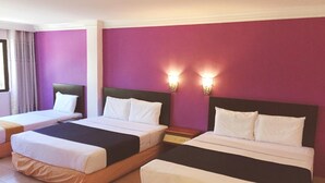 Habitación de hotel con dos camas individuales, cada una con cabecero de madera y ropa de cama blanca. Las paredes están pintadas de morado y hay dos lámparas fijadas a la pared.