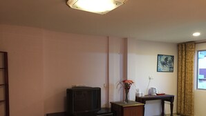 Una sala de estar con televisor sobre un mueble de madera, una mesita con un jarrón de flores y un cuadro en la pared.