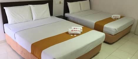 Two twin beds with white and orange bedding, a small table with a Raja Inn towel, and a plain white wall.