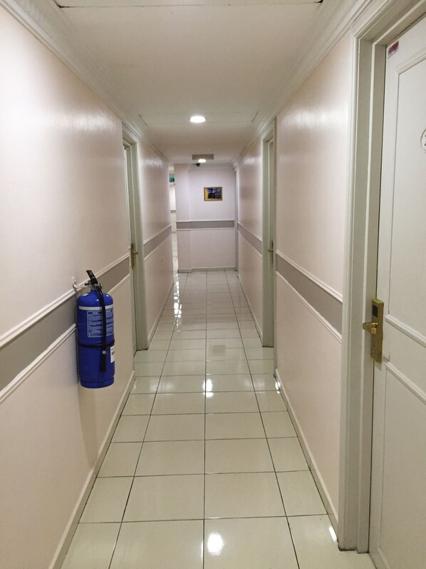 A hallway with white walls, a blue fire extinguisher, and a door on the right.