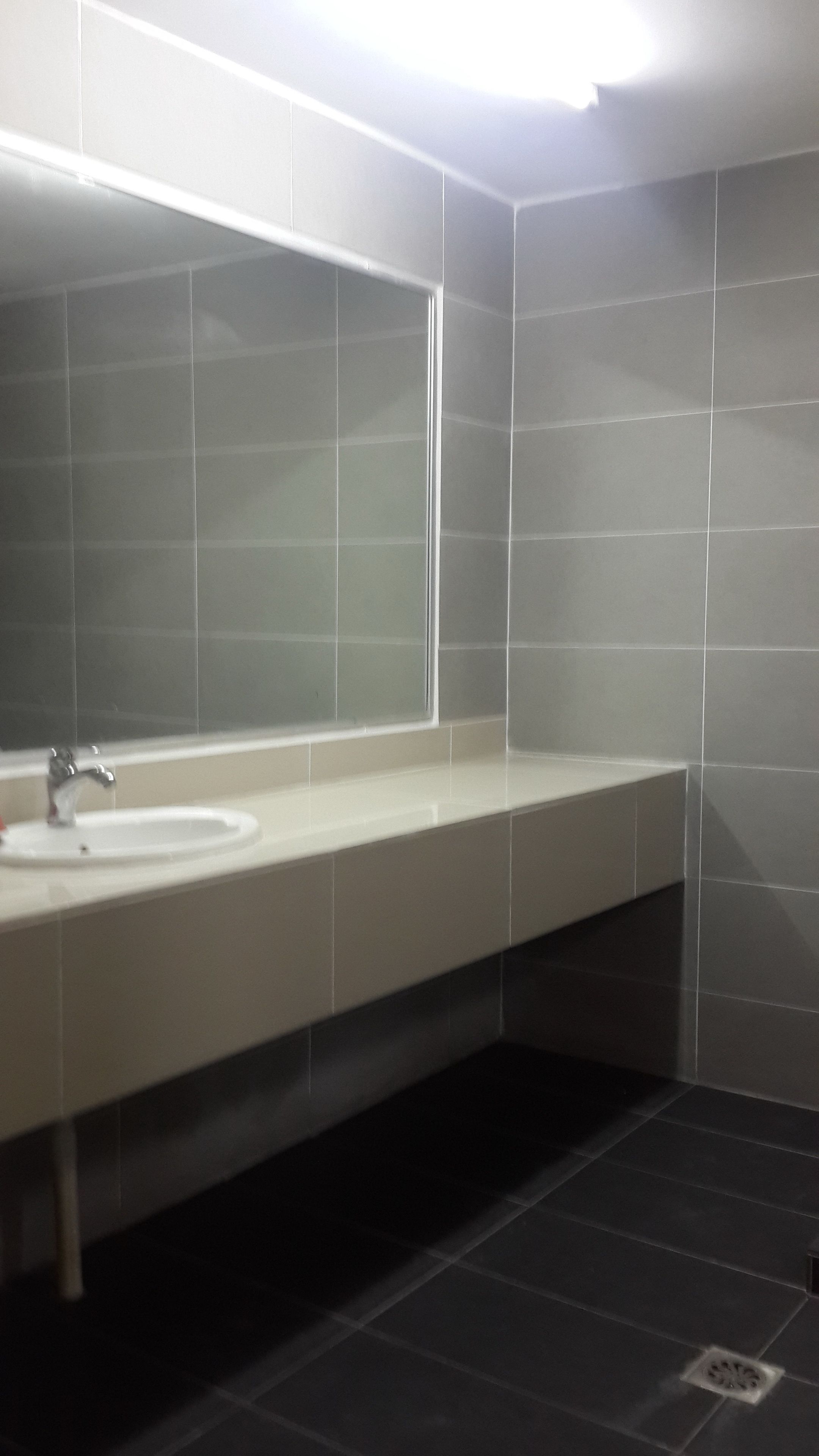 A modern bathroom with a large mirror, a sink, and dark tiled walls.