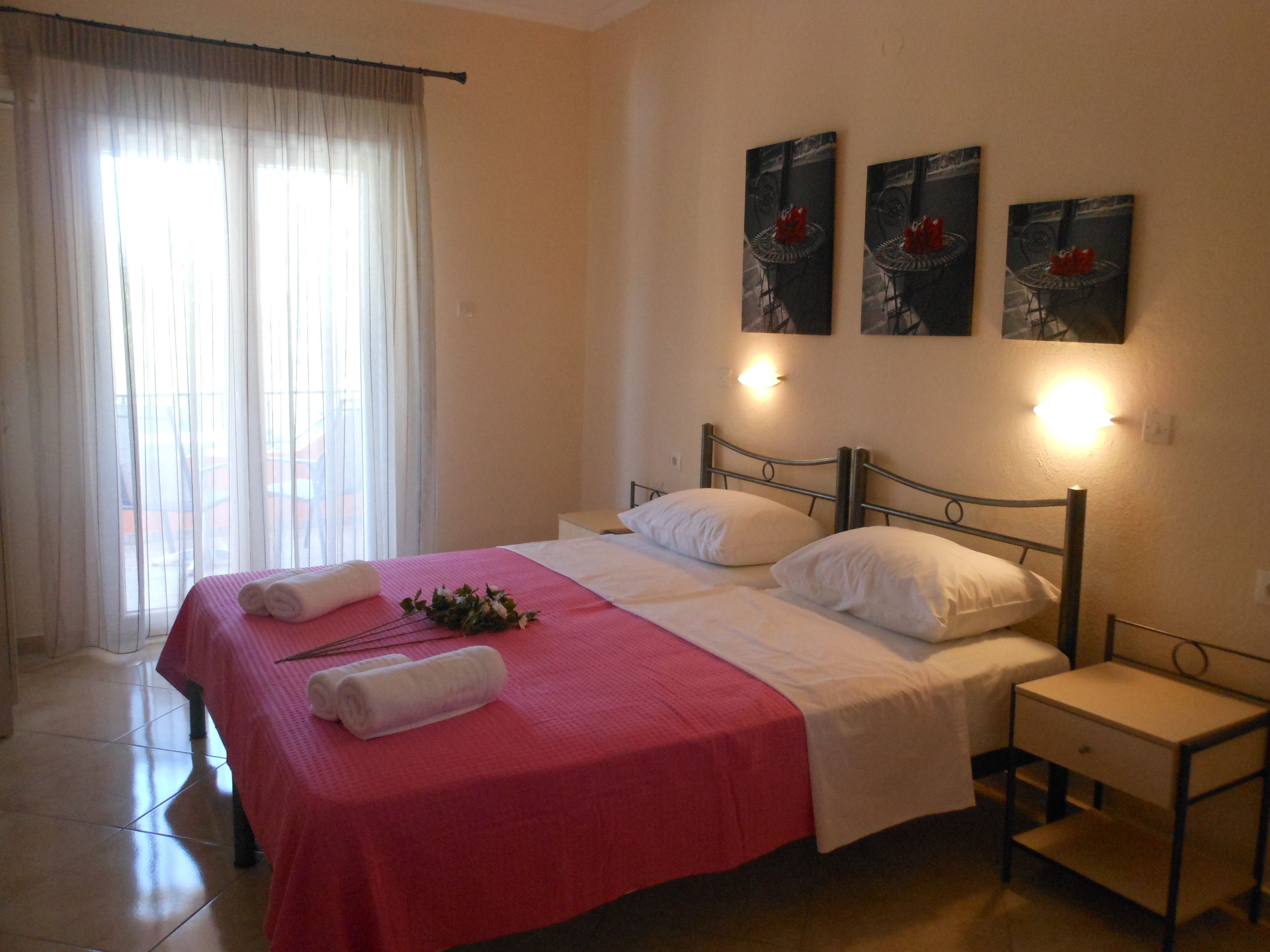 A hotel room with a bed, a nightstand, a window with curtains, and wall-mounted artwork.