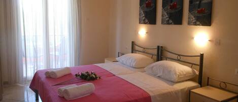 A hotel room with a bed, a nightstand, a window with curtains, and wall-mounted artwork.