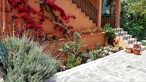 A building with a staircase, potted plants, and a stone-paved area. - Ziogas Apartments (Corfu)