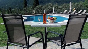 A poolside table with two chairs, a bottle, and a bowl of fruit. - Ziogas Apartments (Corfu)