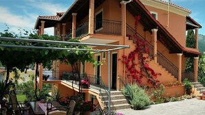 A two-story building with a balcony, a staircase, and a car parked in front. - Ziogas Apartments (Corfu)