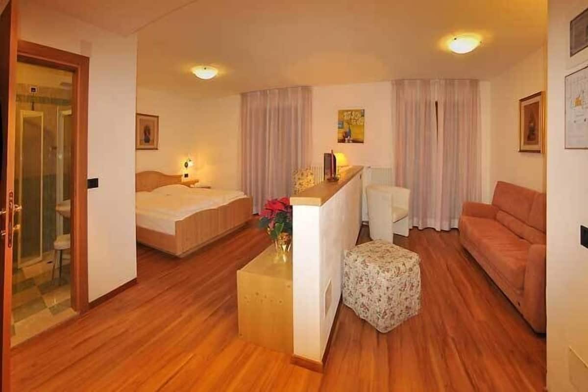A hotel room with a bed, a sofa, a small table with a vase, and a desk with a lamp.