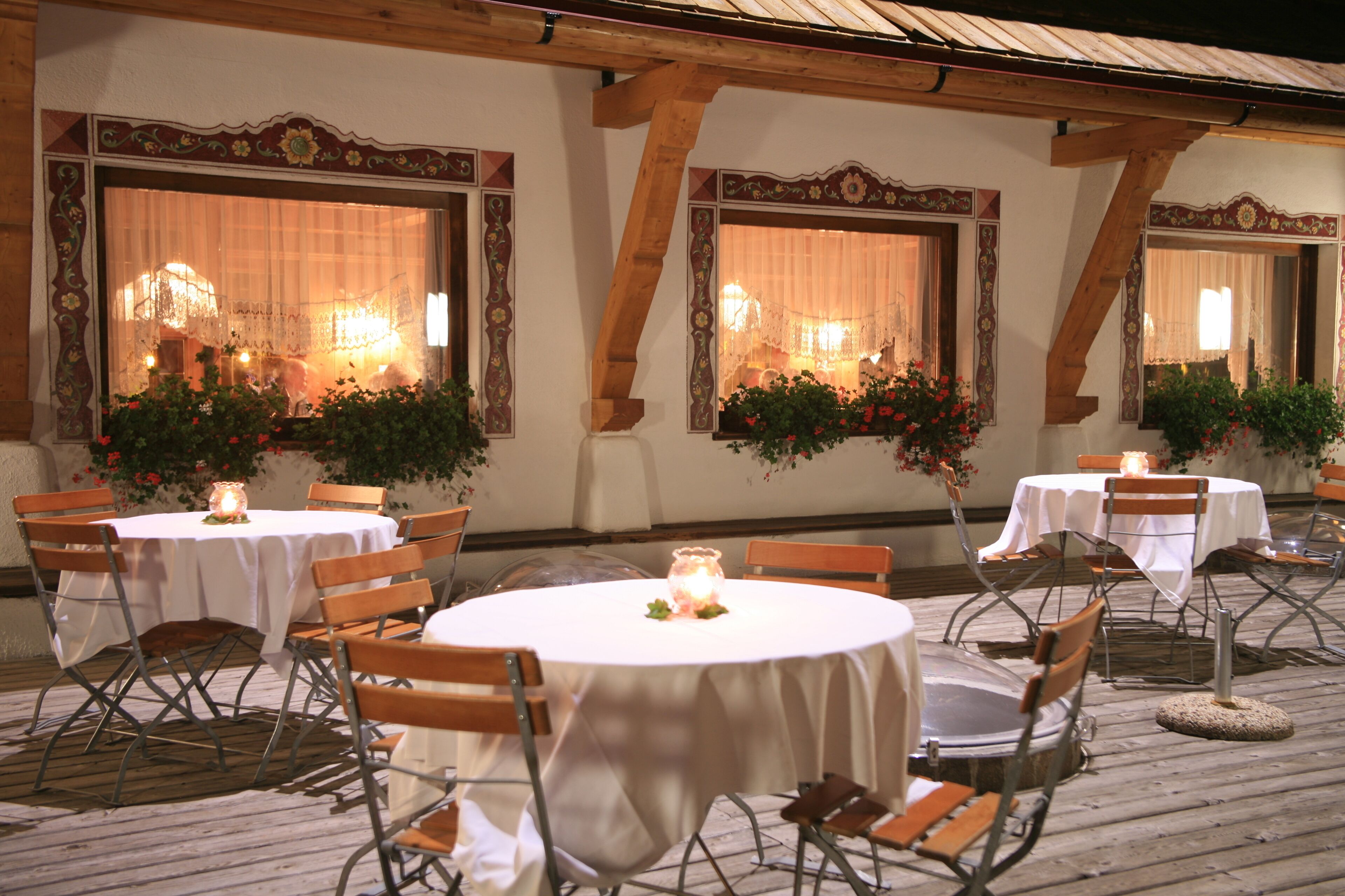 An outdoor dining area with round tables and chairs, decorated with candles and flowers.