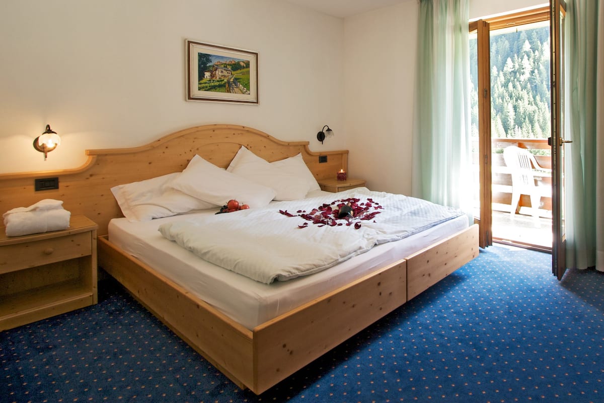 A neatly made bed with white linens and pillows, a wooden headboard, a small bedside table with a lamp, and a painting on the wall.