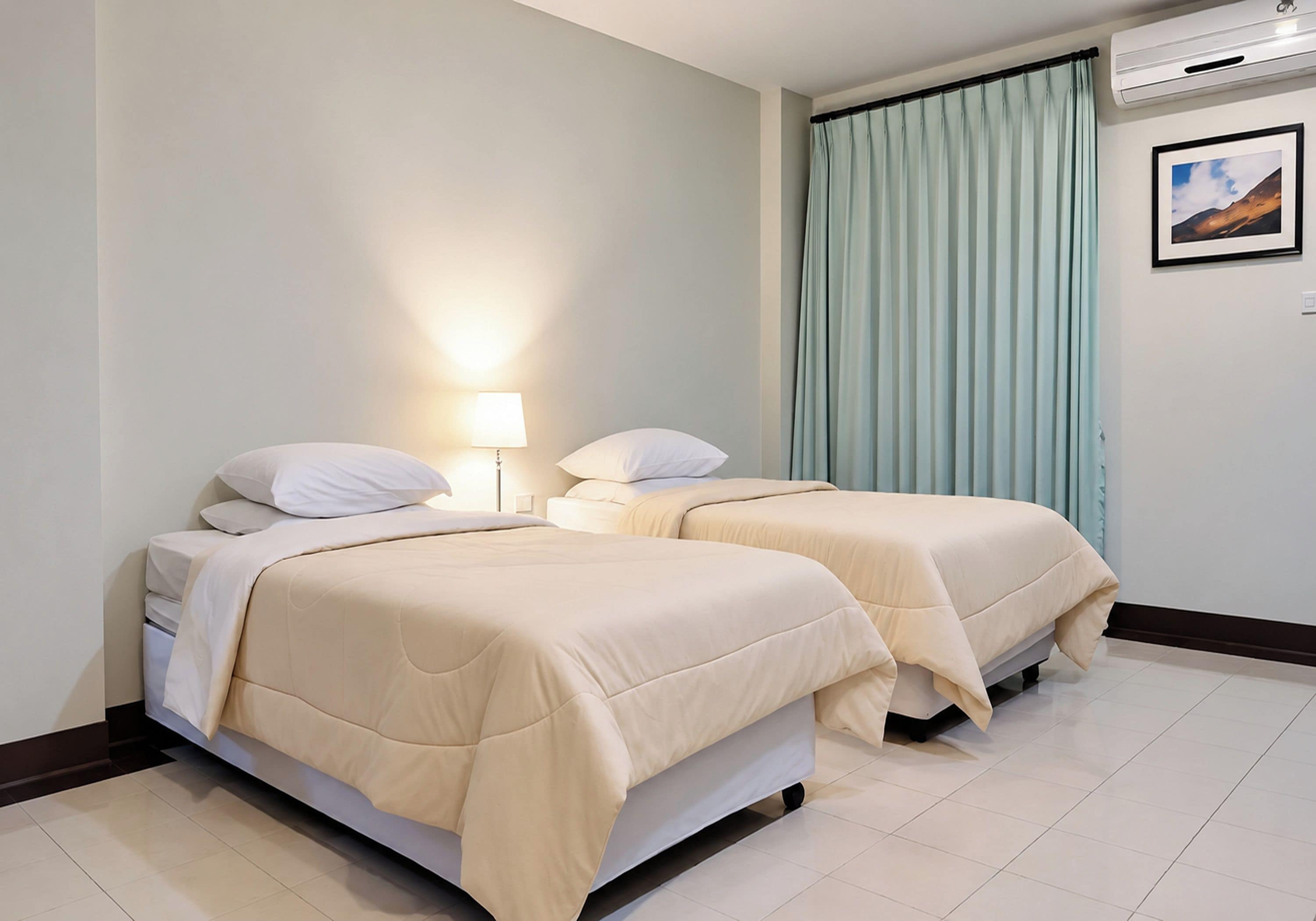 A hotel room with two beds, a nightstand, a lamp, a window with curtains, and a wall-mounted air conditioner.