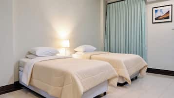 Una habitación de hotel con dos camas, una mesita de noche, una lámpara, una ventana con cortinas y un aire acondicionado instalado en la pared.