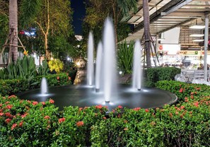 A fountain surrounded by greenery and a building with signage in the background. - Udoncabana (Udon Thani)