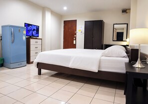 A hotel room with a bed, a television, a wardrobe, and a desk with a lamp.