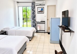 Ein Hotelzimmer mit zwei Betten, einem Schreibtisch mit Computer, einem Fernseher und einem Fenster mit Vorhängen.