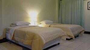 Een hotelkamer met twee bedden, een nachtkastje, een lamp en een raam met gordijnen.
