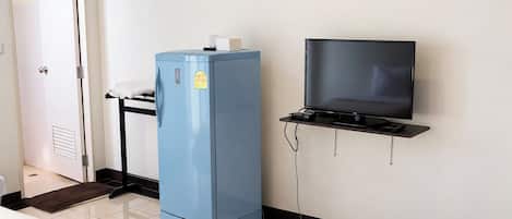 Une pièce avec un lit, un réfrigérateur bleu, un téléviseur posé sur un meuble et une porte.