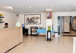 A reception area with a wooden reception desk, a computer, a framed artwork, and a vase with flowers. - Udoncabana (Udon Thani)