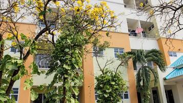 Un edificio de varios pisos con balcones, ventanas amplias y una variedad de plantas, incluyendo árboles y arbustos.