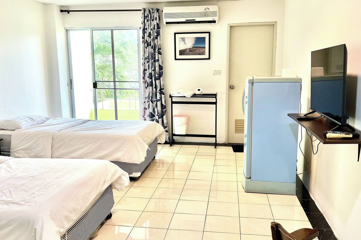Habitación de hotel con dos camas, un escritorio con computadora, televisor y ventana con cortinas.