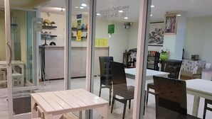 Een kamer met een witte tafel en twee stoelen, een receptiebalie en een muur met een ingelijst schilderij en een groen bord.