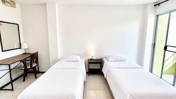 Ein Hotelzimmer mit zwei Einzelbetten, einem Schreibtisch mit Stuhl, einem Nachttisch mit Lampe und einem großen Fenster.