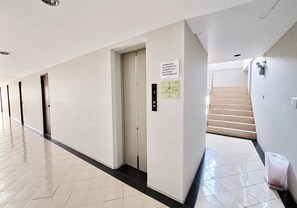 A hotel corridor with a tiled floor, a closed elevator, and a staircase leading to another floor.