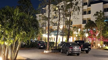 Un estacionamiento con varios autos, un edificio con balcones y árboles.