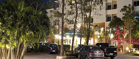 A parking area with multiple cars, a building with balconies, and trees.