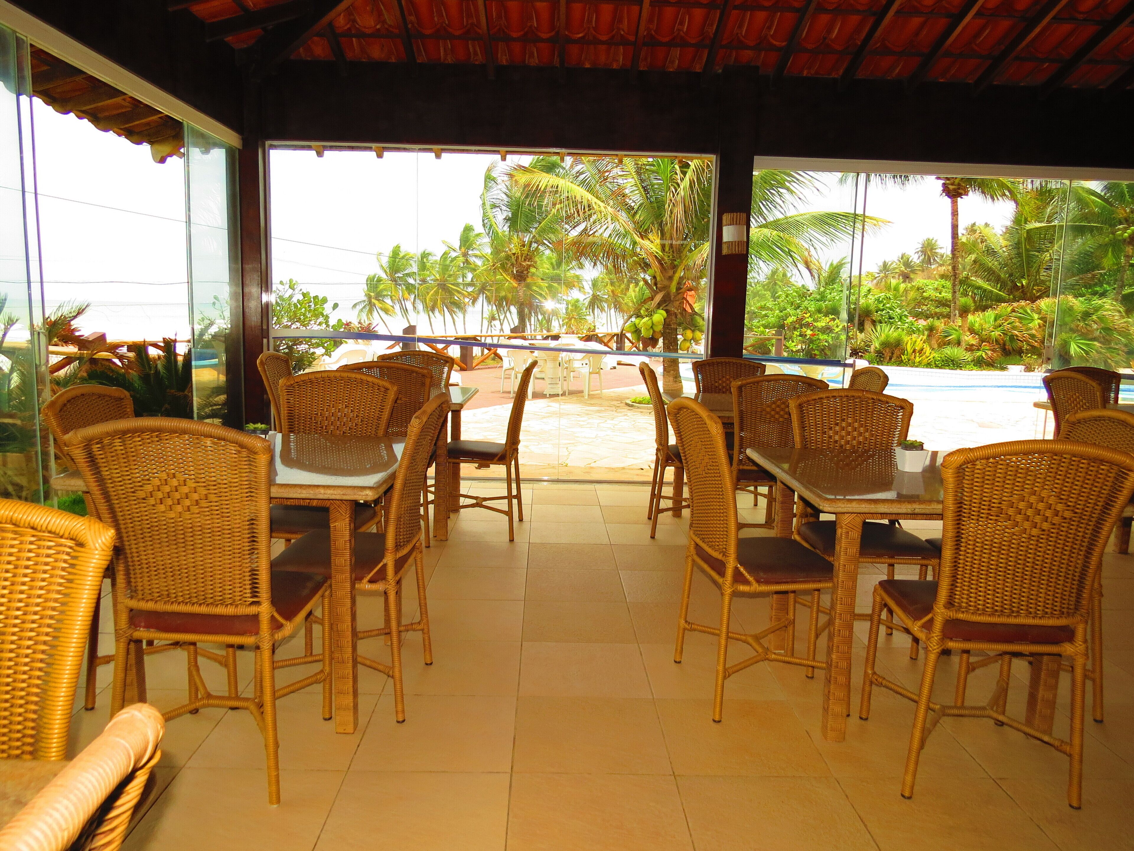 A covered outdoor seating area with wicker furniture and a view of a pool and palm trees.