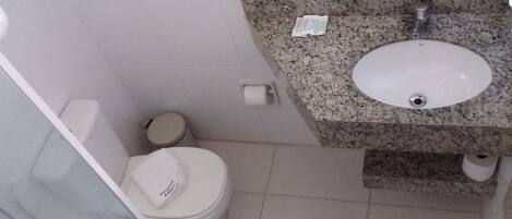 Une salle de bain avec des toilettes blanches, un lavabo en granit et une cabine de douche en verre.