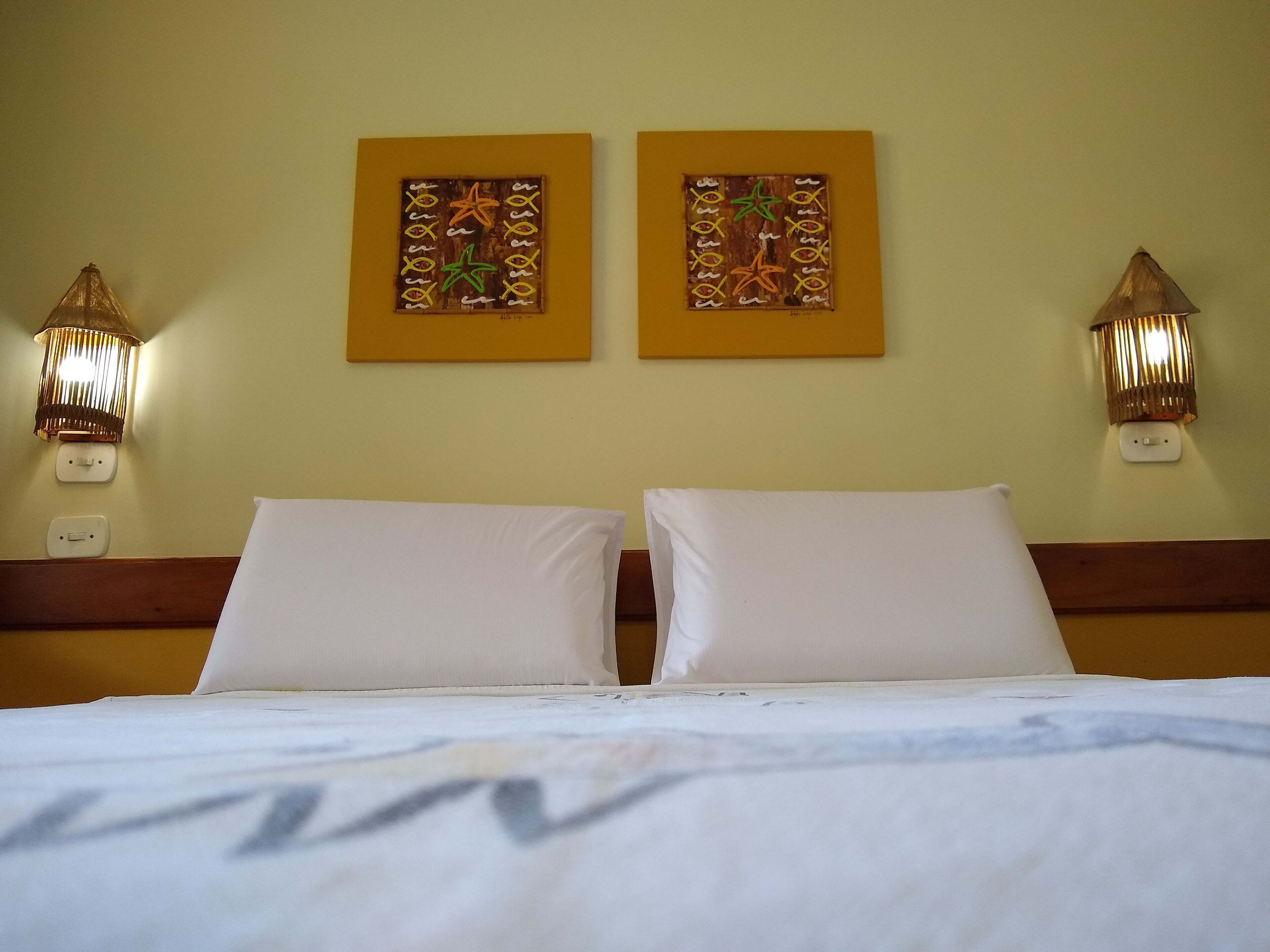 A hotel room with two beds, a wooden headboard, wall-mounted artwork, and two wall sconces.