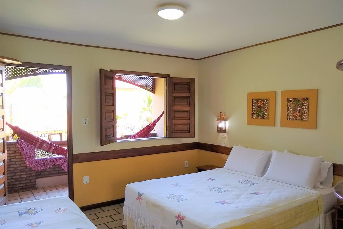 A hotel room with a bed, a small table, a window with a view of the outside, and two wall-mounted artworks.