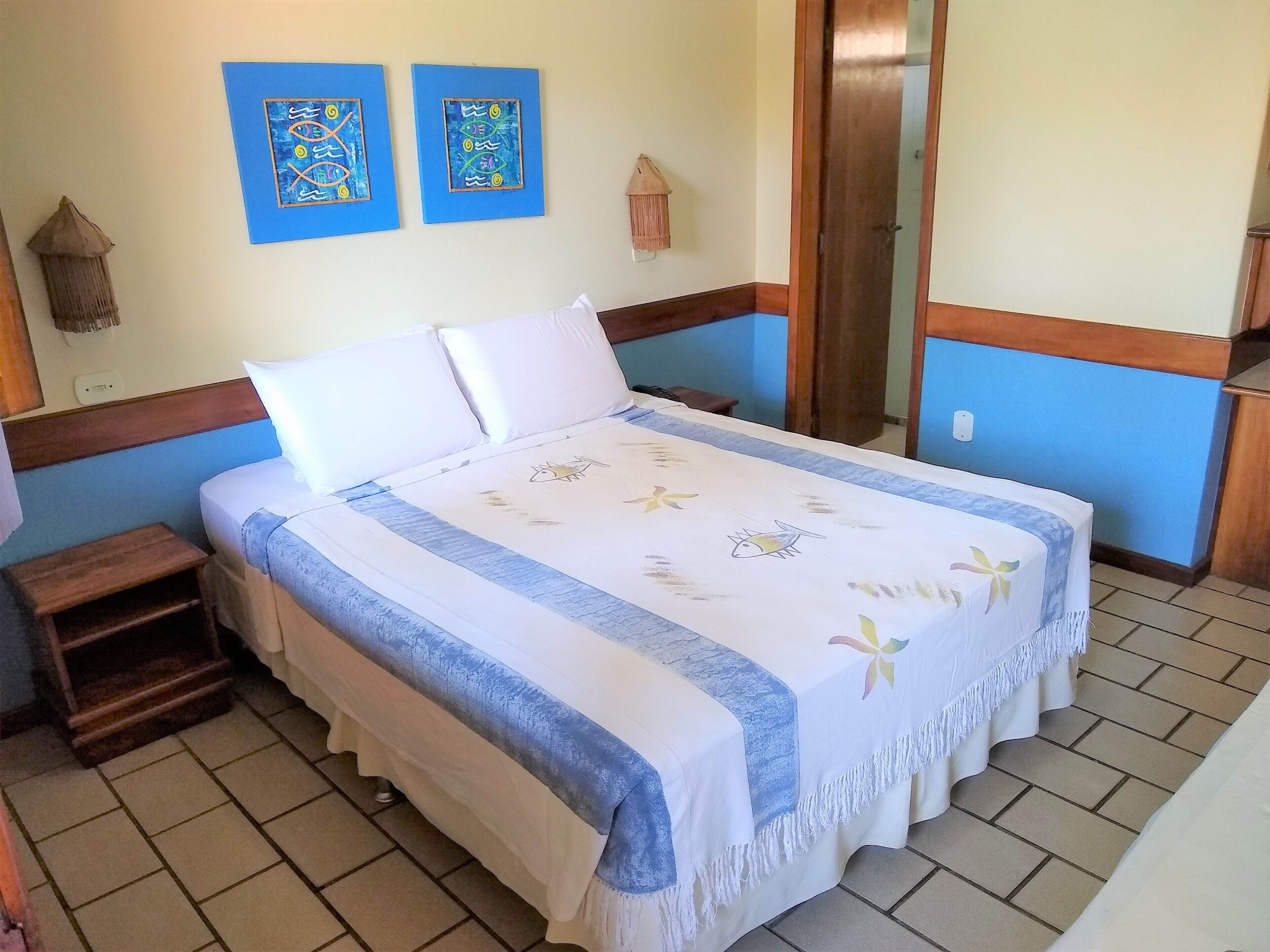 A bedroom with a bed, a small wooden nightstand, a wall-mounted shelf, and two wall art pieces.