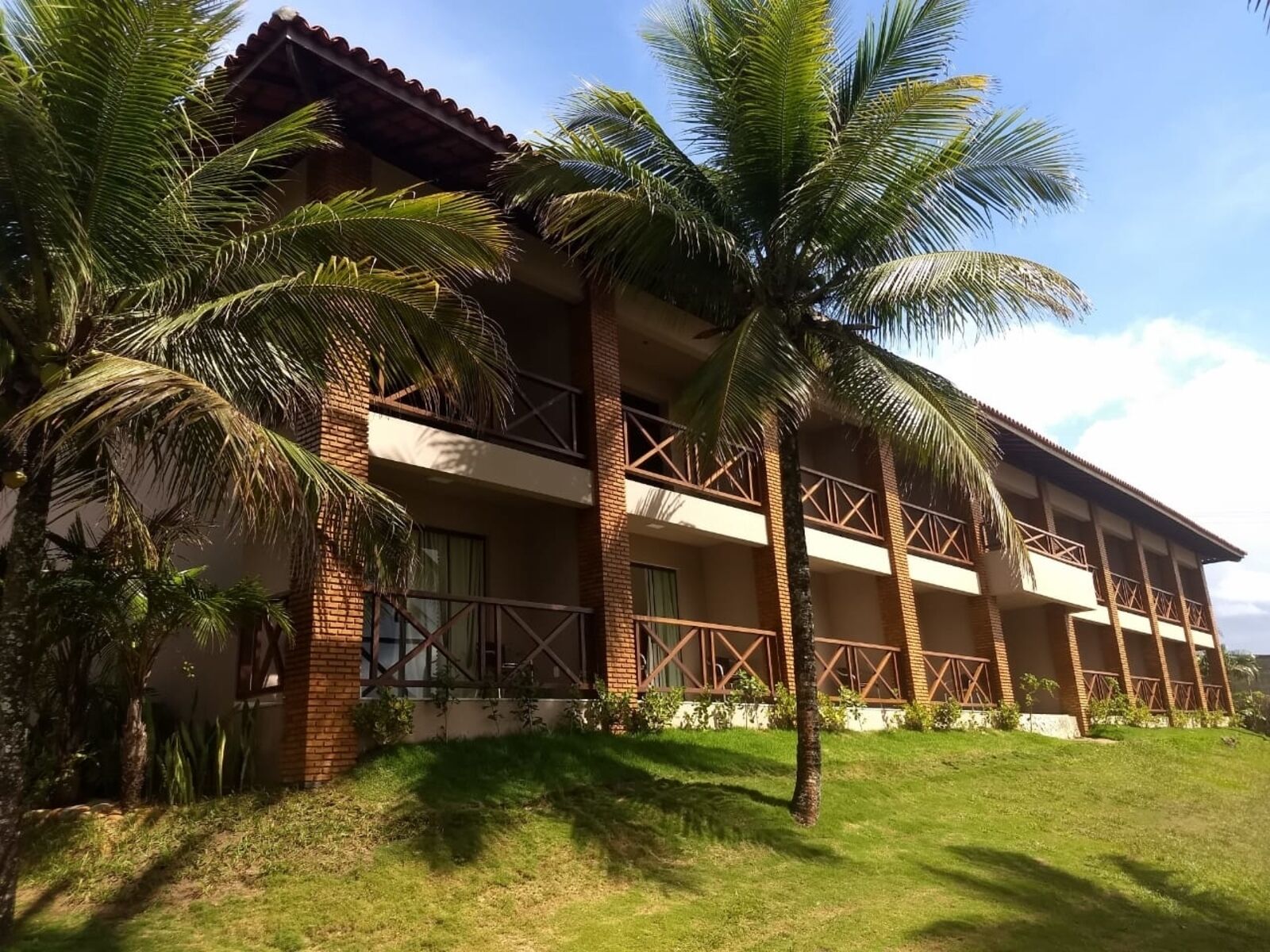 A multi-story hotel with a brick facade, balconies, and palm trees in the foreground.