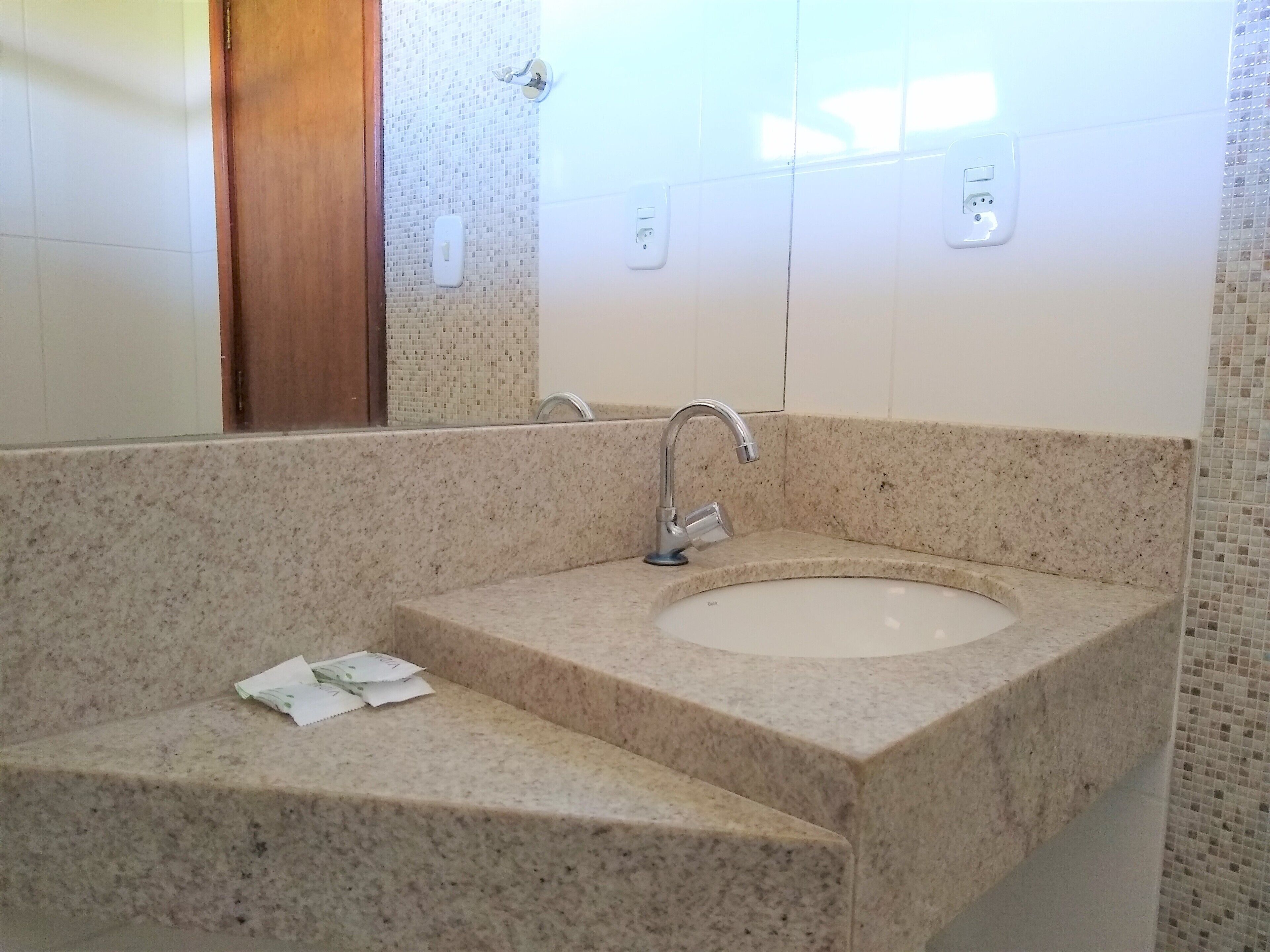 Un baño con lavamanos de encimera de granito, espejo y puerta de madera.