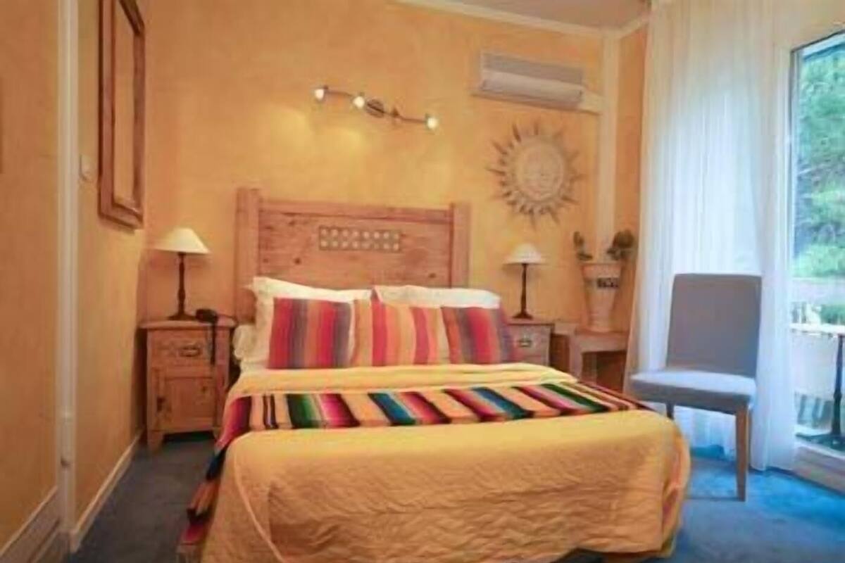 A hotel room with a bed, bedside lamps, a chair, a window, and a wall clock.