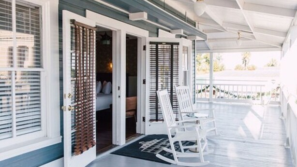 A covered porch with white rocking chairs and a door leading to a bedroom. - Gibson Inn (Apalachicola)