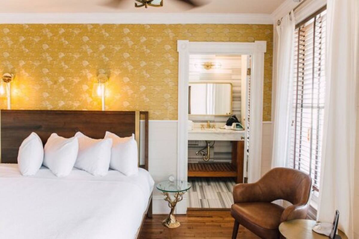 A hotel room with a bed, a chair, a small table, and a bathroom visible through an open door.