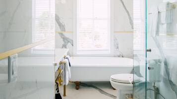 Un baño moderno con suelo de mármol, cabina de ducha de vidrio, bañera blanca y un inodoro.