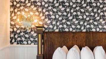 A bedroom with a patterned wallpaper, a wooden headboard, and a bedside table with shoes.