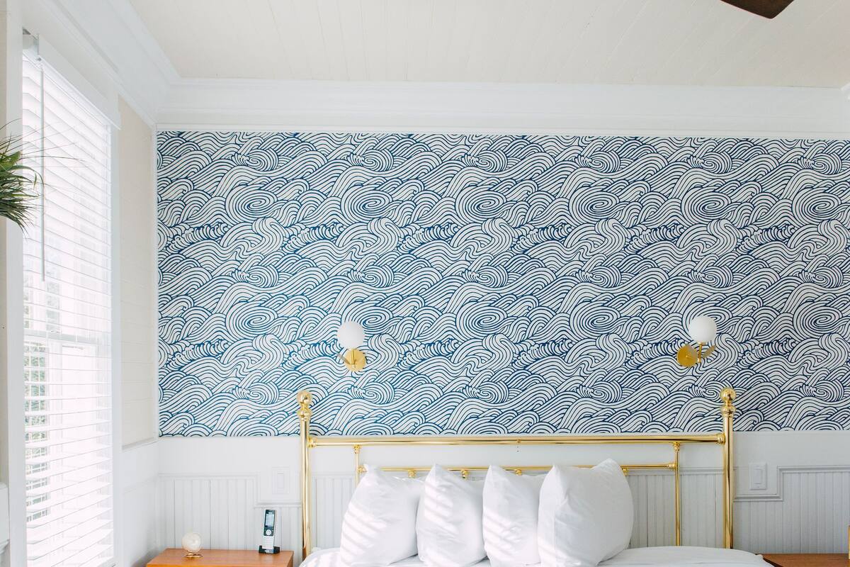 A bedroom with a bed, two chairs, a nightstand, a wall with a blue and white pattern, and a ceiling fan.