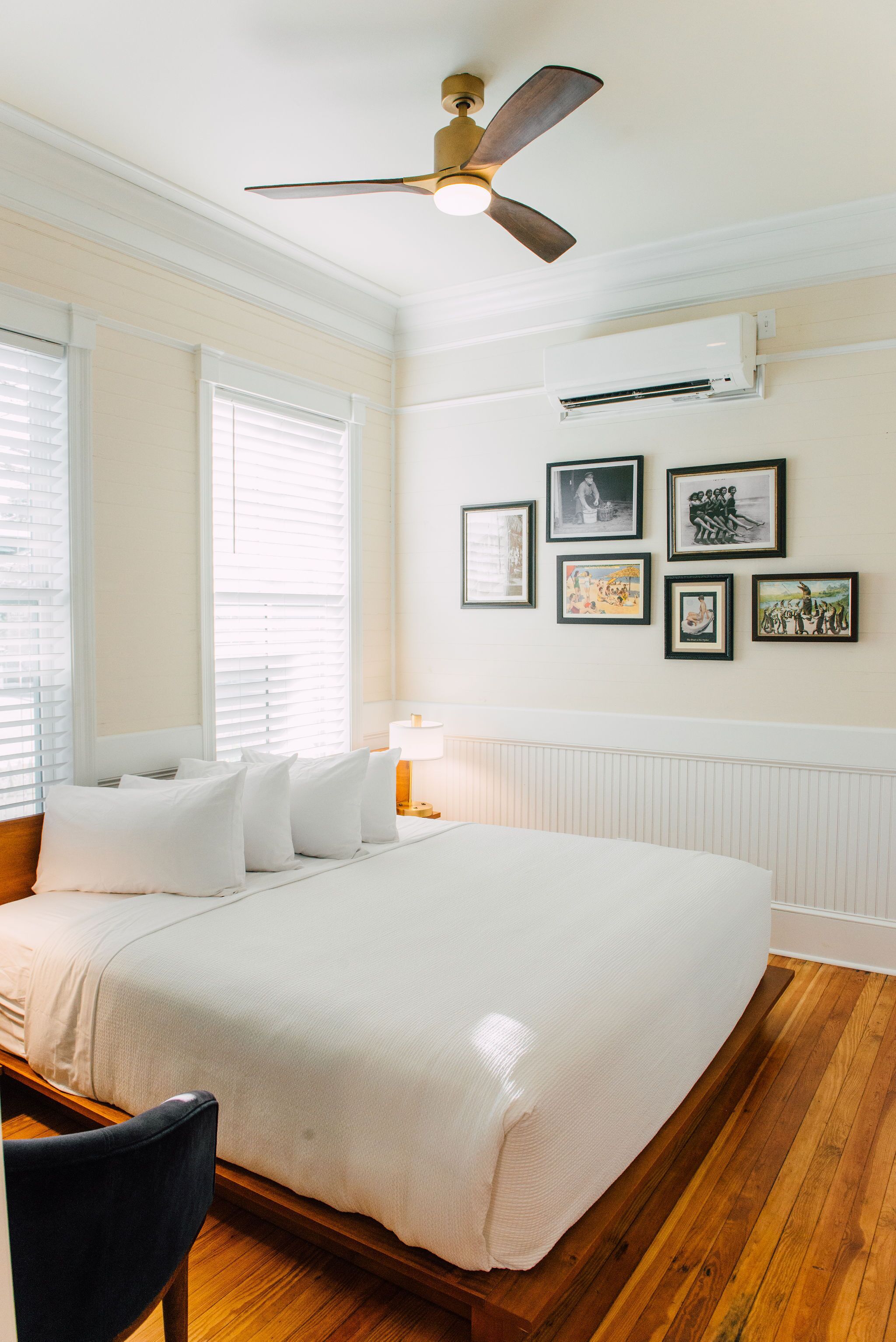 A bedroom with a large bed, a ceiling fan, and framed pictures on the wall.