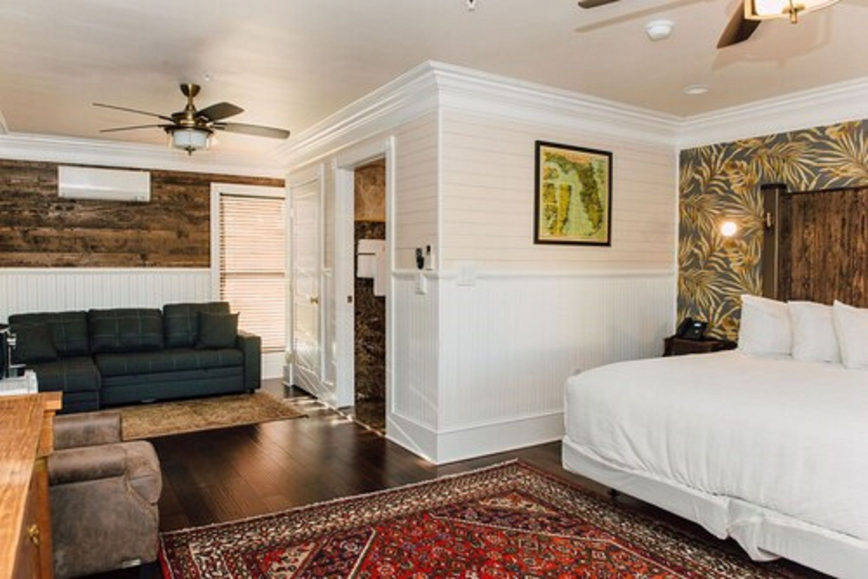 A bedroom with a large bed, a ceiling fan, a dark-colored sofa, and a patterned rug.