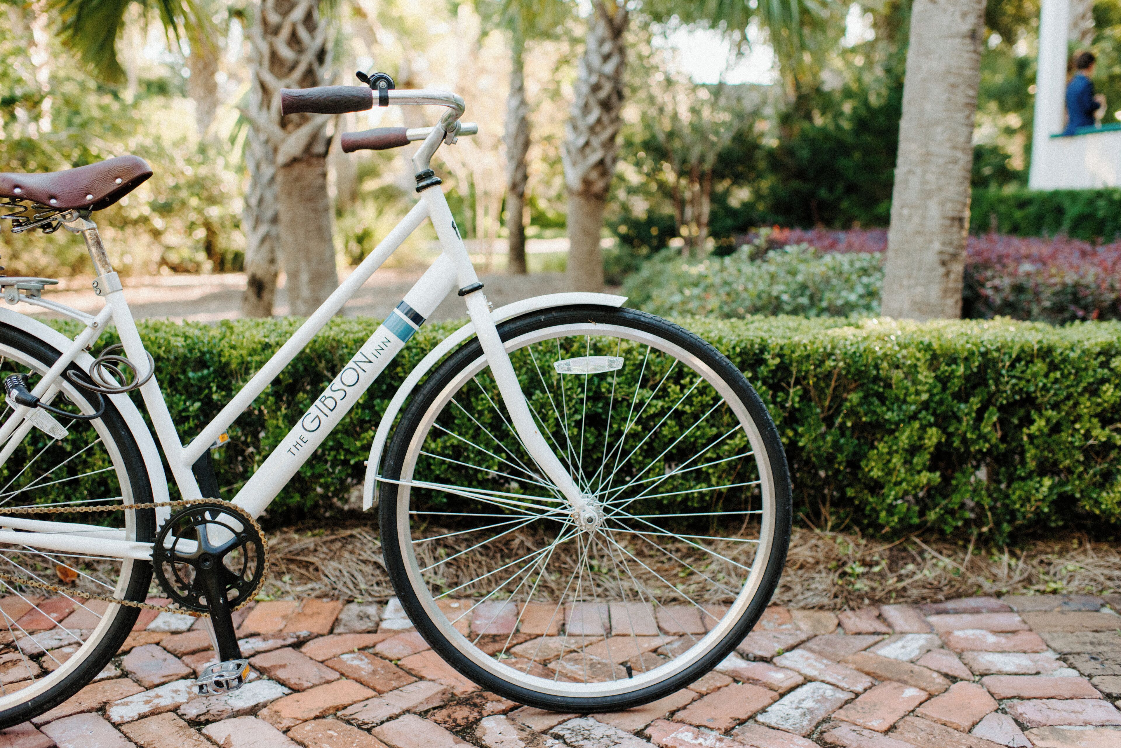 A white bicycle with a chain and a seat, parked on a brick path.