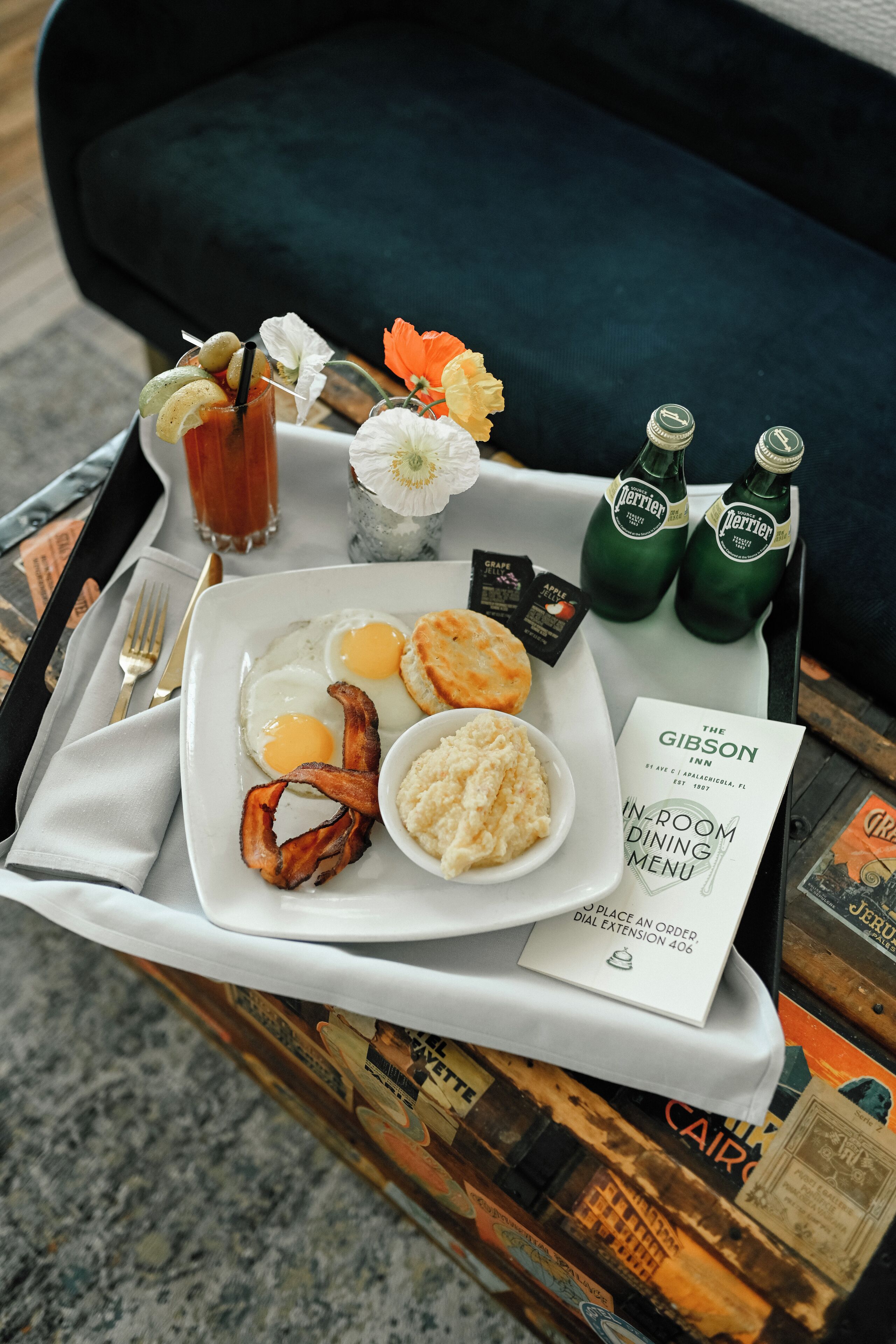 Ein Tablett mit Frühstücksartikeln, darunter Eier, Speck, Kekse und Soße, zusammen mit Perrier-Wasserflaschen und einer Speisekarte für The Gibson Inn.