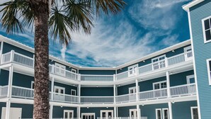 A poolside area with lounge chairs and a palm tree, a multi-story building with balconies, and a clear blue sky. - Gibson Inn (Apalachicola)
