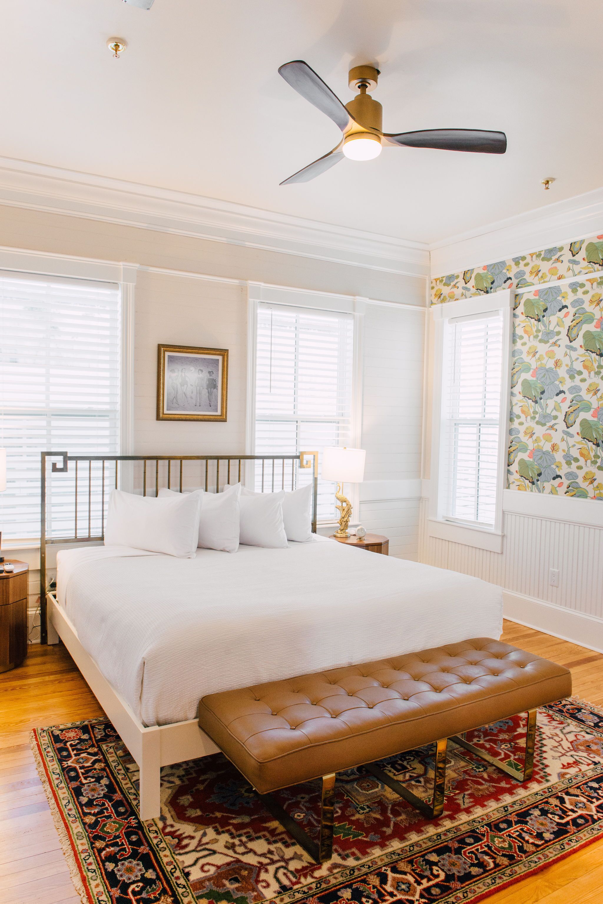 A bedroom with a bed, a bench, a ceiling fan, and a patterned wall.