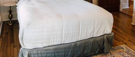 Een groot bed met hoofdeinde, een plafondventilator en een vloerkleed met dessin.