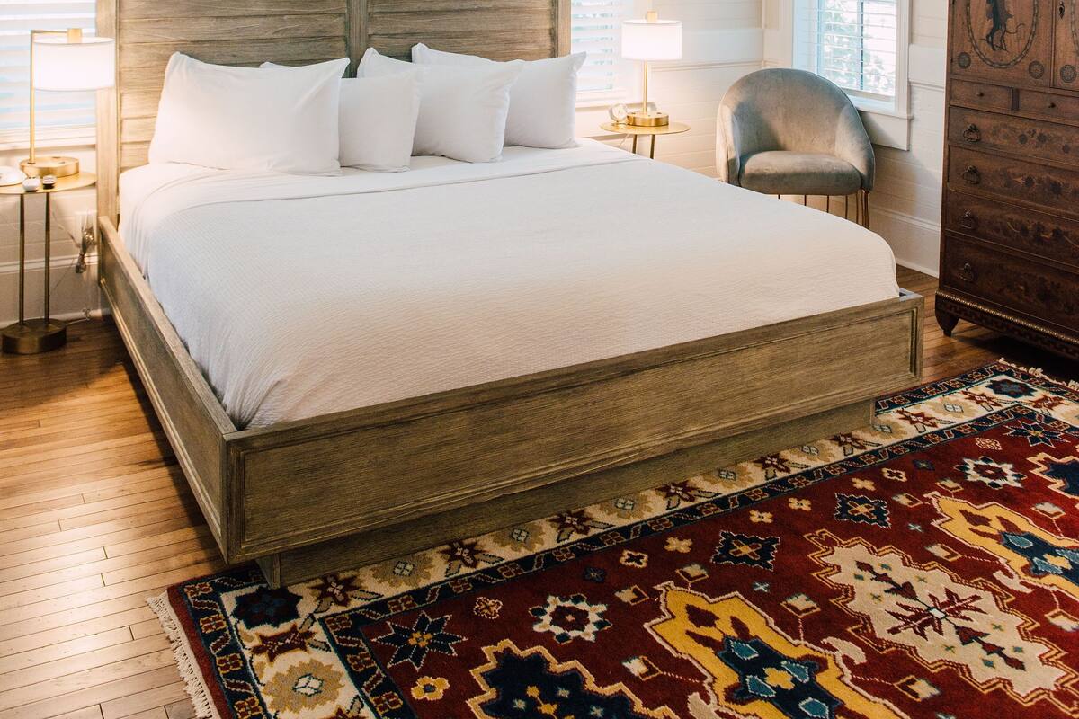 A bedroom with a wooden bed, a ceiling fan, a patterned rug, and a nightstand with a lamp.